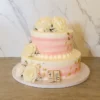 Delicado pastel de dos pisos con un suave diseño de líneas difuminadas en tonos blanco y rosa pastel. Está hermosamente decorado con destellos de hoja de oro, abundantes rosas blancas con pequeñas flores nube y un sutil librito de fondant en la base que dice "Mi Primera Comunión". Castillo's Cake Shop.