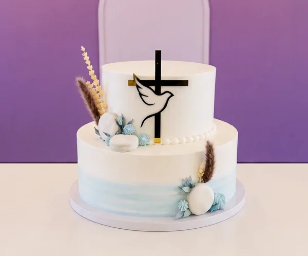 Sofisticado pastel de dos pisos con un suave degradado en acuarela color azul claro en la base. Su diseño celestial incluye una cruz negra con una paloma blanca en acrílico, macarrones blancos, estrellitas de glaseado azul, hojitas de fondant y sutiles espigas secas en tonos tierra y azulados. Castillo's Cake Shop.