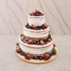 Bodas5 Pastel de bodas de tres pisos con un diseño rústico estilo "semi-desnudo" (semi-naked), que deja entrever el bizcocho a través de una fina capa de glaseado blanco. Está abundantemente adornado con frutos rojos frescos, incluyendo fresas, arándanos y frambuesas, todo cubierto con un espolvoreado de azúcar glass.