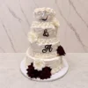 Bodas8 Sofisticado pastel de bodas de cuatro pisos cubierto con fondant blanco. Está elegantemente decorado con guirnaldas y bordes estilo Lambeth. Presenta las iniciales "L & A" en letras acrílicas de espejo plateado oscuro. El contraste se logra con hermosas rosas en tono rojo vino en la base y el piso inferior, complementadas con rosas blancas.