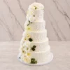 Bodas9 Majestuoso pastel de bodas de cinco pisos con glaseado blanco que luce un patrón espatulado rústico en toda la superficie. El diseño destaca por una hermosa y tupida cascada de flores blancas, incluyendo rosas y lirios, acompañadas de follaje verde oscuro que fluye desde la parte superior hasta la base.
