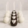 Elegantes cake pops con temática formal o de boda organizadas en tres filas. La primera fila está cubierta de chocolate blanco con un diseño de líneas diagonales texturizadas. La fila central presenta un diseño de esmoquin con chocolate oscuro, pechera blanca, botones y un pequeño moño. La tercera fila está completamente cubierta de chocolate blanco y adornada con diminutas chispas redondas.
