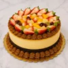Exquisito pastel redondo tipo "chocoflan" o pastel imposible, que combina una base de pan de chocolate oscuro con una gruesa capa central de flan cremoso. Está bellamente rematado con bordes de rosetones de dulce de leche y una corona de frutas frescas mixtas como fresas, mango y uvas. Castillo's Cake Shop.