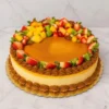 Delicioso cheesecake redondo con una cubierta lisa de dulce de leche o caramelo. Sus bordes superior e inferior están decorados con rosetones de dulce de leche, y luce un colorido arreglo en forma de media luna con frutas frescas picadas (fresas, mango, kiwi y uvas). Castillo's Cake Shop.