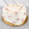 Clásico y romántico pastel en forma de corazón con cobertura blanca pura. Está hermosamente decorado con volutas, guirnaldas y bordes de glaseado blanco estilo vintage, acentuado a lo largo de su diseño con delicadas rosas de glaseado rosa pastel y sutiles hojas verdes. Castillo's Cake Shop.