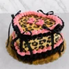 Llamativo pastel en forma de corazón con un audaz diseño de estampado de leopardo en la superficie y los costados. Los bordes están decorados con rosetones de glaseado en color rosa y negro profundo, acentuados con elegantes lazos de cinta negra satinada y el número "22" en color rosa en el centro. Castillo's Cake Shop.