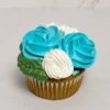 Cupcake clásico decorado con un hermoso arreglo floral de glaseado, que incluye dos vibrantes rosas color azul turquesa, flores blancas y hojas verdes entrelazadas. Castillo's Cake Shop.