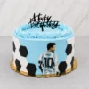 Pastel redondo cubierto de glaseado azul celeste con bordes acanalados en la parte superior. Los costados tienen un diseño parcial de balón de fútbol con hexágonos de fondant. Al frente destaca una imagen de Lionel Messi de espaldas con la camiseta número 10 de Argentina, rematado con un letrero negro de "Happy Birthday". Castillo's Cake Shop.