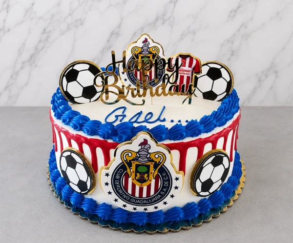 Pastel redondo con temática del equipo Chivas. Cubierta blanca con un goteo (drip) rojo vibrante y gruesos bordes de rosetones azules. Decorado con escudos del Club Deportivo Guadalajara, balones, una camiseta del equipo en la parte superior, el nombre "Gael" en glaseado azul y un letrero dorado de "Happy Birthday". Castillo's Cake Shop.