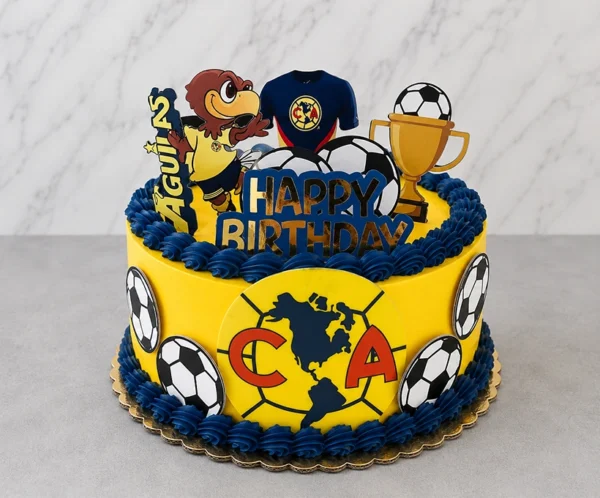 Pastel redondo en color amarillo brillante con bordes de rosetones azul marino, inspirado en el Club América. El frente luce un gran escudo del equipo, acompañado de imágenes de balones en los costados. La parte superior está decorada con la mascota del equipo, una camiseta, un trofeo dorado y un letrero de "HAPPY BIRTHDAY" en azul y dorado. Castillo's Cake Shop.