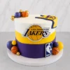 Elegante pastel cilíndrico con los colores de Los Angeles Lakers: franjas gruesas en blanco, amarillo y morado. En el centro lleva el logotipo de los Lakers y el escudo de la NBA en la base. Está decorado con esferas en morado, amarillo, dorado y pequeñas pelotas de básquetbol, además del detalle de la camiseta con el número 23 sobre el borde superior. Castillo's Cake Shop.