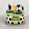 Pastel con cubierta verde lisa y bordes de glaseado que simulan césped. Los laterales muestran un patrón parcial de balón de fútbol con hexágonos blancos y negros. Decorado al frente con un letrero dorado caligráfico de "Happy Birthday", y en la cima con recortes de los nombres "ISAIAH" y "ANDRE", un gran balón, un trofeo y la figura de Cristiano Ronaldo. Castillo's Cake Shop.