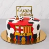 Pastel redondo con cubierta roja vibrante, adornado en los costados con hexágonos blancos y negros de fondant formando la clásica textura de un balón. Al frente destaca un gran escudo del FC Barcelona. En la parte superior lo decoran tres pequeños balones de fútbol y un letrero cuadrado dorado que dice "happy BIRTHDAY". Castillo's Cake Shop.
