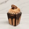 Ferrero en vasito. Elegante postre servido en un vasito cuadrado transparente. Se compone de una base de mousse o crema de chocolate con llamativos escurrimientos de jarabe de chocolate oscuro en el interior del vaso. La superficie está decorada con un gran rosetón de crema de chocolate claro y la mitad de un clásico chocolate Ferrero Rocher con avellanas.