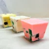 Gelatina 3 leches en vasito. Tres vasitos transparentes cuadrados que contienen gelatina de tres leches estilo mosaico. El primer vaso tiene una base de gelatina color rosa, el del medio es de color blanco y el del fondo es amarillo pálido. En su interior flotan coloridos cubos de gelatina de agua (verde, rojo y oscuro).
