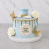 Elegante pastel redondo con glaseado azul claro pastel y un llamativo escurrimiento (drip) dorado. Está bellamente decorado con rosas blancas, mariposas doradas en 3D, un birrete azul claro con diploma en la parte superior, y una placa frontal rodeada de pequeños rosetones blancos con detalles dorados que dice "CONGRATS YOSELIN CLASS OF 2025". Castillo's Cake Shop.