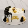 ofisticado pastel redondo con un diseño asimétrico. Tiene una base blanca con un dramático escurrimiento (drip) de chocolate negro que cubre la mitad izquierda. La corona está dividida por ondas de crema blanca: un lado presenta fresas cubiertas de chocolate oscuro con hoja de oro, y el otro chocolates Ferrero Rocher y perlas doradas. Al frente luce un letrero de "Happy Birthday", acompañado de racimos de esferas negras y doradas en la base. Castillo's Cake Shop.