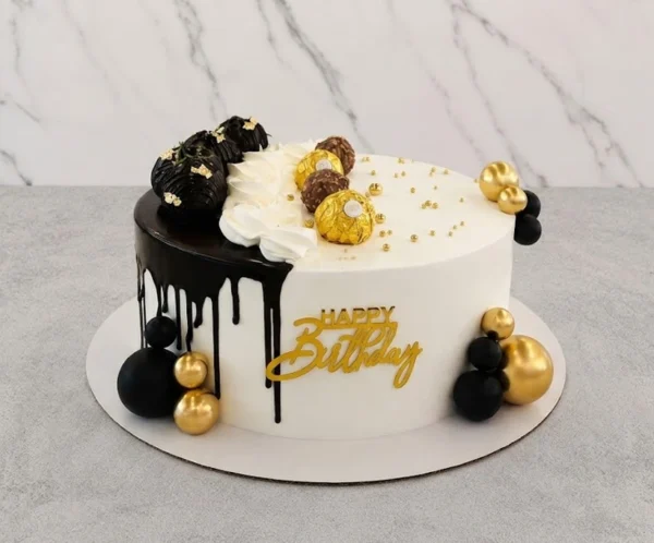 ofisticado pastel redondo con un diseño asimétrico. Tiene una base blanca con un dramático escurrimiento (drip) de chocolate negro que cubre la mitad izquierda. La corona está dividida por ondas de crema blanca: un lado presenta fresas cubiertas de chocolate oscuro con hoja de oro, y el otro chocolates Ferrero Rocher y perlas doradas. Al frente luce un letrero de "Happy Birthday", acompañado de racimos de esferas negras y doradas en la base. Castillo's Cake Shop.