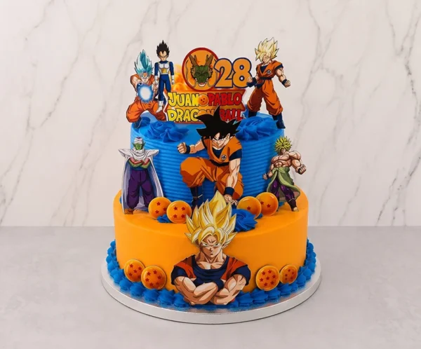 Pastel de dos pisos con temática de Dragon Ball. El piso inferior es de color naranja brillante con bordes de rosetones azules, decorado con las esferas del dragón y una figura central de Goku. El piso superior es azul con textura de líneas horizontales. La decoración superior incluye figuras de Goku, Vegeta, Piccolo, Broly, Shenlong y un letrero personalizado que dice "28 Juan Pablo Dragon Ball". Castillo's Cake Shop.