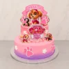Pastel de dos pisos con temática de Skye de Paw Patrol. La cubierta tiene un degradado que va de rosa a morado en la base. El piso inferior está decorado con huellitas rosas y flores blancas. El piso superior y la parte superior lucen figuras de Skye, el logo de Paw Patrol, el número "3" texturizado, bordes de rosetones rosas y un letrero superior con el nombre "CAMILA". Castillo's Cake Shop.