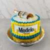 Divertido pastel redondo diseñado para simular una hielera. Los laterales están cubiertos con una etiqueta comestible de Cerveza Modelo Especial, enmarcada por gruesos rosetones entrelazados en colores amarillo y azul intenso. La parte superior está cubierta con cubos de gelatina transparente que imitan hielos, sobre los cuales descansa una botella real de Cerveza Modelo semi-inclinada. Castillo's Cake Shop.
