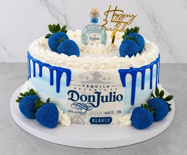 Pastel redondo con un suave diseño en tonos blanco y azul difuminado, destacando un vibrante escurrimiento (drip) azul oscuro. En el frente luce la etiqueta comestible de Tequila Don Julio Blanco. Está decorado con fresas bañadas en una brillante cobertura azul metálica con destellos, rosetones de crema blanca, un letrero dorado de "Happy Birthday" y una botella miniatura real de Don Julio en la corona. Castillo's Cake Shop.