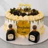Lujoso pastel redondo con cobertura crema suave y un elegante escurrimiento (drip) dorado brillante. Al frente presenta una gran etiqueta comestible de Tequila Don Julio Añejo. La parte superior está adornada con un anillo de rosetones de crema con perlas doradas y fresas frescas bañadas en chocolate oscuro, acompañadas de un letrero dorado de "Happy Birthday". En la base flanquean dos botellas miniatura reales de Tequila Don Julio. Castillo's Cake Shop.