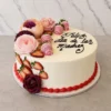 Mujer1 Pastel redondo con cobertura blanca y un borde inferior de glaseado rojo. Está decorado con hermosas flores en tonos rosa y durazno, fresas frescas (algunas de ellas bañadas en chocolate rosa con líneas blancas) y el mensaje "Feliz dia de las Madres" escrito en elegante caligrafía negra. Castillo's Cake Shop.