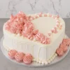 Mujer2 Romántico pastel en forma de corazón con glaseado blanco y un sutil escurrimiento (drip) de chocolate blanco. Está bellamente adornado con una cascada de rosetones de glaseado rosa en distintos tamaños, complementado con un diseño de perlas de azúcar en colores blanco y rosa suave. Castillo's Cake Shop.
