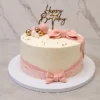 Mujer6 Sofisticado pastel redondo de cobertura blanca, envuelto en su base con una cinta de fondant rosa que termina en un pequeño moño, y coronado con un moño rosa de fondant mucho más grande y estructurado. Está decorado con un elegante arreglo de esferas doradas, blancas y rosas, perlas doradas y un topper de acrílico de "Happy Birthday". Castillo's Cake Shop.