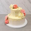 Mujer8 Hermoso pastel de dos pisos con cobertura en tono crema claro y un escurrimiento (drip) de chocolate a juego en ambos niveles. Su decoración es clásica y elegante, conformada por preciosas rosas de glaseado en colores rosa y crema, acentuadas con sutiles destellos de hoja de oro. Castillo's Cake Shop.