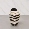 Oreo en vasito. Postre en capas servido en un vasito transparente cuadrado. Intercala gruesas líneas de polvo oscuro de galleta triturada con una crema clara moteada. Se corona con un abundante rosetón de crema sabor cookies and cream y la mitad de una galleta Oreo tradicional.