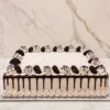 Pastel de Oreo Rectangular Pastel de formato rectangular con glaseado tipo cookies and cream (con pequeñas motas de galleta triturada), textura estriada y goteo de chocolate oscuro. Todo el perímetro superior está adornado con rosetones de glaseado decorados con finos hilos de chocolate y mitades de galleta Oreo incrustadas.