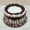 Pastel de Oreo Redondo 1 Pasteles redondos cubiertos con glaseado de cookies and cream con textura de líneas horizontales y un goteo de chocolate oscuro profundo. En la parte superior destacan mitades de galletas Oreo entrelazadas formando un círculo interior, rodeadas por rosetones de glaseado. El borde inferior está rematado con rosetones y migajas de galleta Oreo espolvoreadas.