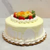 Pastel de Tres Leches 2 Pastel redondo cubierto con glaseado blanco de textura estriada y un delicado goteo continuo de chocolate blanco o ganache. En el centro superior destaca una colorida y abundante mezcla de frutas frescas (fresas, kiwi y durazno), rodeada por un borde clásico de rosetones de glaseado blanco.