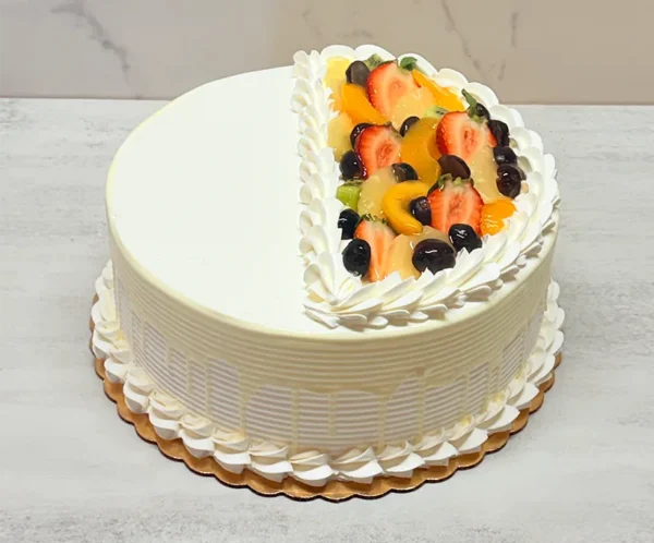 Pastel de Tres Leches 3 Pastel redondo con glaseado blanco texturizado y goteo del mismo tono. Su diseño superior está creativamente dividido por una media luna de rosetones blancos: una mitad se mantiene lisa, mientras que la otra exhibe una colorida mezcla de fresas, duraznos, kiwi y uvas oscuras o arándanos.