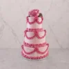 PastelXV_5 Pastel de tres pisos en tono rosa pastel con un exquisito diseño de glaseado estilo Lambeth. Decorado con elaborados drapeados, bordes de concha y detalles entrelazados en un rosa más intenso, acentuados con finos hilos blancos y perlas de azúcar. Rematado en la corona con una hermosa rosa natural.