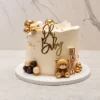 Pastel redondo de un piso con cobertura lisa en tono crema. Está decorado con un tierno osito de fondant, cubos de juguete que forman la palabra "BABY", y un hermoso arreglo de esferas de chocolate en tonos dorado metálico, blanco y café. En la parte superior luce un letrero dorado de "Oh Baby". Castillo's Cake Shop.