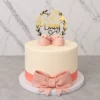 Elegante pastel redondo de un piso con cobertura lisa en color crema. En la base destaca un listón y un gran moño de fondant en color rosa viejo. Está coronado con un par de tiernos zapatitos de bebé en fondant rosa y un delicado adorno dorado con corona de laureles que dice "Oh Baby". Castillo's Cake Shop.