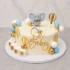 Pastel redondo de un piso con base crema, decorado con una tierna temática de elefantito. Incluye un arreglo de esferas en tonos azul claro, blanco y dorado, siluetas doradas de globos aerostáticos, cubos con las letras "B A B Y", un elefantito de fondant en la parte superior y un letrero dorado de "Oh Baby". Castillo's Cake Shop.