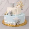 Pastel de dos pisos con temática de elefantitos. El piso inferior es color azul cielo pastel con nubes blancas y cubos que dicen "B A B Y". El piso superior es blanco con estrellas doradas y una escalerita blanca apoyada en el borde. Está decorado con tres adorables elefantes grises de fondant en diferentes posiciones, esferas en tonos blanco, gris y dorado, y un letrero superior de "Oh Baby". Castillo's Cake Shop.