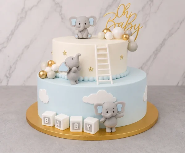 Pastel de dos pisos con temática de elefantitos. El piso inferior es color azul cielo pastel con nubes blancas y cubos que dicen "B A B Y". El piso superior es blanco con estrellas doradas y una escalerita blanca apoyada en el borde. Está decorado con tres adorables elefantes grises de fondant en diferentes posiciones, esferas en tonos blanco, gris y dorado, y un letrero superior de "Oh Baby". Castillo's Cake Shop.